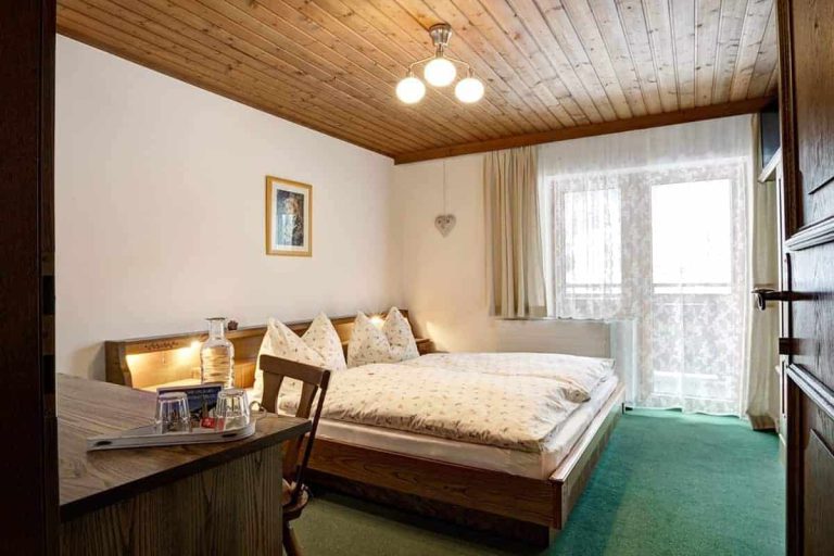 Gemütliches Doppelzimmer mit Holzmöbeln, Balkonzugang und Tageslicht in der Pension Forsthof